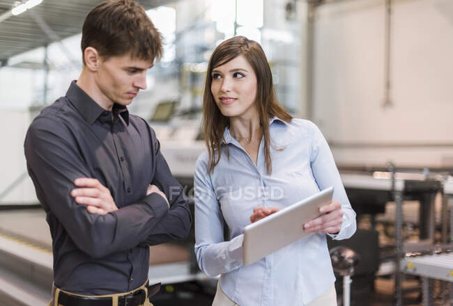 Donna d'affari che mostra tablet digitale al collega maschio mentre in piedi in fabbrica — Foto stock