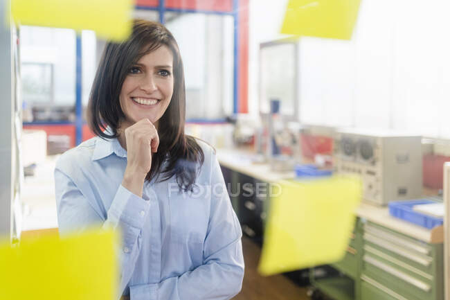 Portrait of a smiling businesswoman looking at adhesive notes in a factory office — Stock Photo