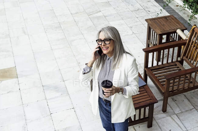 Усміхнена старша жінка-підприємець дивиться геть, розмовляючи на мобільний телефон в саду — стокове фото
