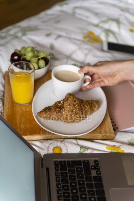 Cropped image of woman with coffee and laptop in bedroom — Stock Photo