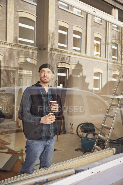 Чоловік ремонтує місце розташування магазину, п'є каву, дивлячись з вікна — стокове фото