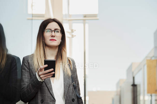 Portrait of young businesswoman with smartphone looking at distance — Stock Photo