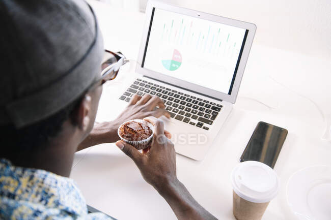 Man using laptop while eating muffin at home — Stock Photo
