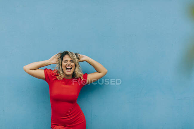 Девушка в красном платье танцует у голубой стены — стоковое фото