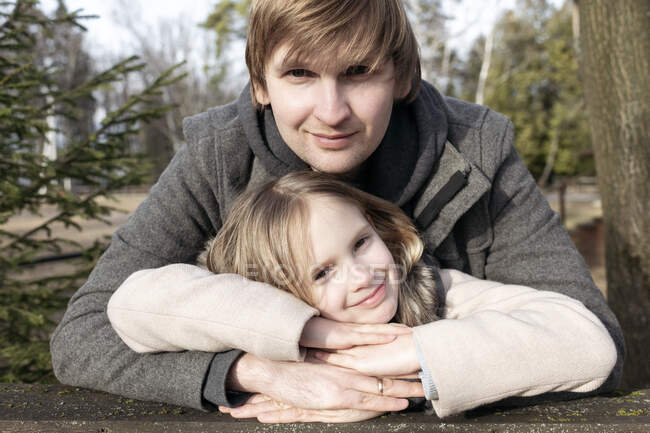 Retrato de niña sonriente apoyada en las manos del padre en el patio trasero durante el día soleado, Tarusa, Rusia - foto de stock