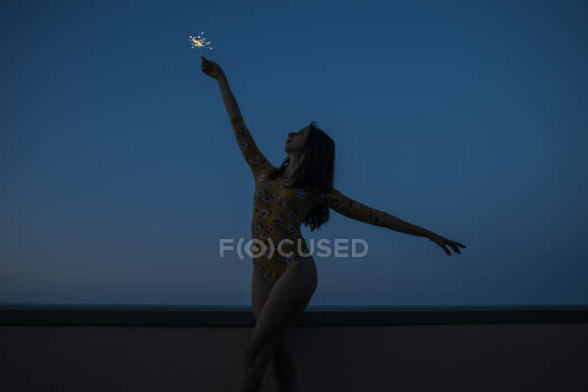 Обережна жінка, що тримає блиск, стоячи на терасі перед ясним блакитним небом під час заходу сонця. — стокове фото