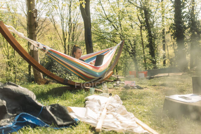 Young woman using laptop while sitting on hammock at yard — Stock Photo