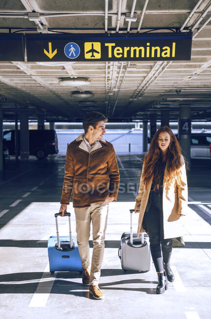 Business couple pulling luggage while walking under terminal sign at airport — Stock Photo