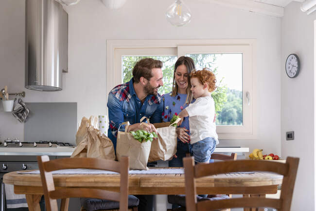 Счастливая семья с продуктовой сумкой за обеденным столом на кухне — стоковое фото