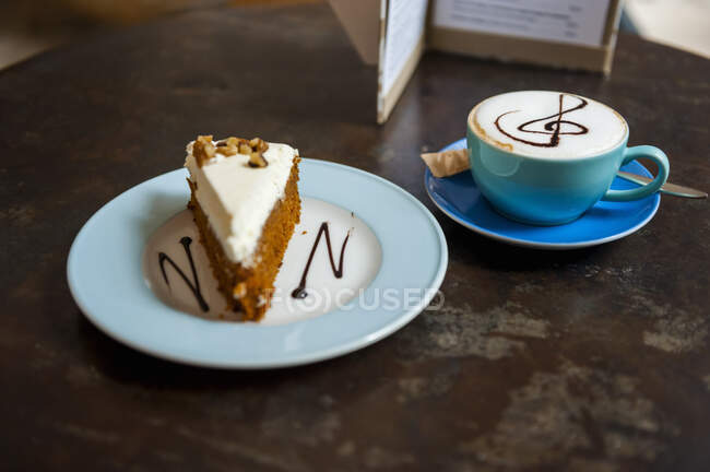 Eine Tasse Cappuchino und ein Stück Kuchen auf dem Tisch in einem Café — Stockfoto