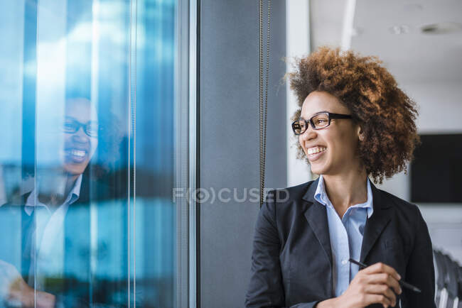 Ritratto di giovane donna d'affari felice in carica che guarda fuori dalla finestra — Foto stock