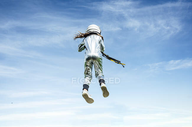 Vista trasera de ángulo bajo de astronauta chica en traje espacial saltando en día soleado - foto de stock