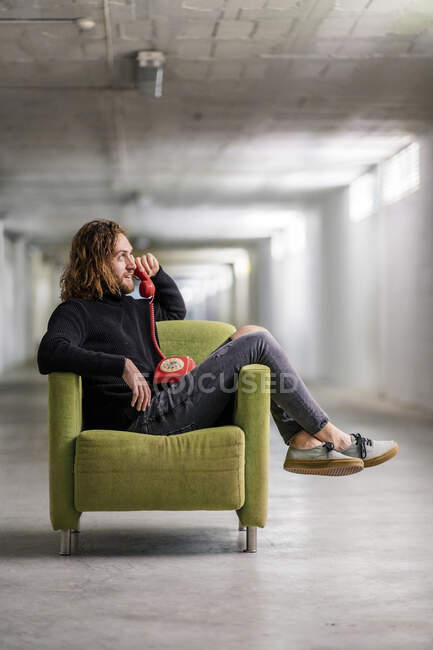 Hombre hablando por teléfono mientras se relaja en el sillón en casa - foto de stock