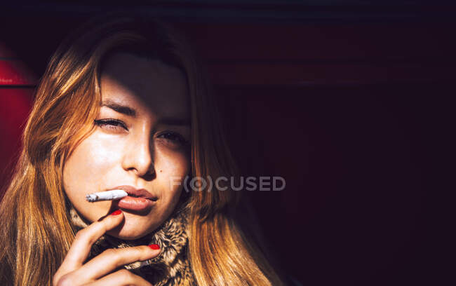 Primo piano della donna d'affari fiduciosa che fuma sigaretta contro il muro in città — Foto stock