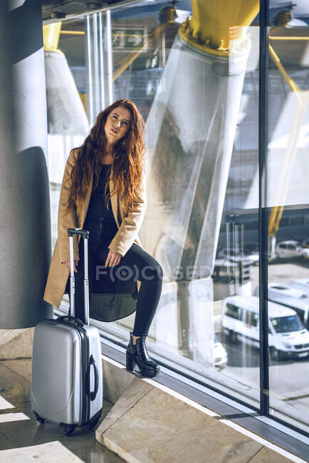 Fiduciosa donna d'affari in piedi con i bagagli alla finestra nell'area di partenza dell'aeroporto — Foto stock