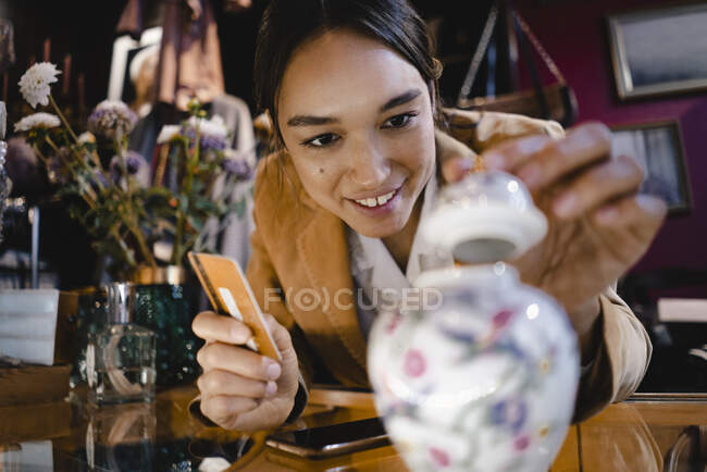 Donna curiosa con carta di credito guardando vaso nel negozio di risparmio — Foto stock