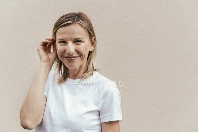 Ritratto di donna bionda sorridente che indossa una t-shirt bianca davanti alla parete chiara — Foto stock