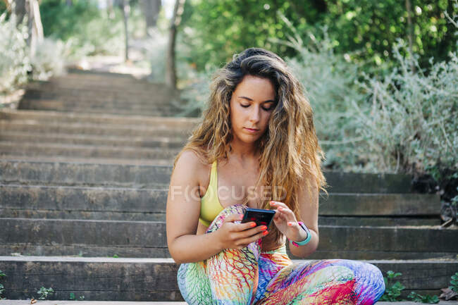 Giovane donna che utilizza smart phone mentre seduto su gradini nel parco — Foto stock