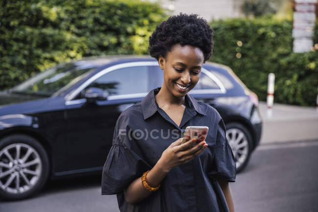 Portrait of smiling young woman standing on the street looking at cell phone — Stock Photo