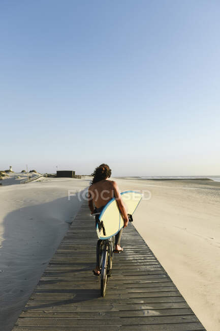 Surfista in bicicletta durante il tramonto, tenendo tavola da surf — Foto stock