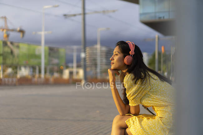 Jeune femme réfléchie écoutant de la musique alors qu'elle était assise en ville — Photo de stock
