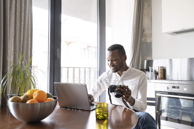 Portrait of smiling man using laptop and camera at home — Stock Photo