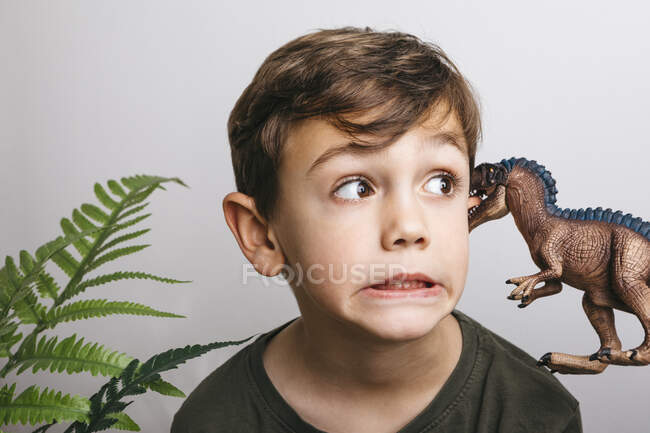 Portrait of little boy with toy dinosaur pulling funny face — Stock Photo