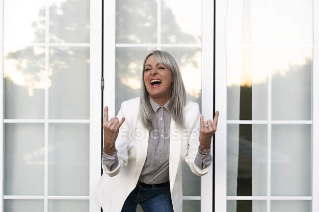 Fröhliche Seniorin zeigt Hupschild, während sie gegen Bürotür steht — Stockfoto