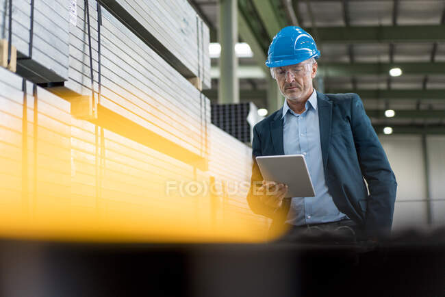 Mature businessman wearing hard hat and safety goggles in a factory using tablet — Stock Photo