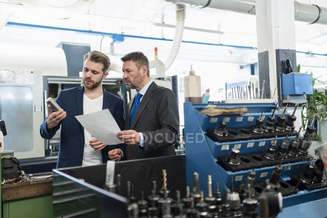 Dos hombres de negocios teniendo una reunión de trabajo en una fábrica - foto de stock