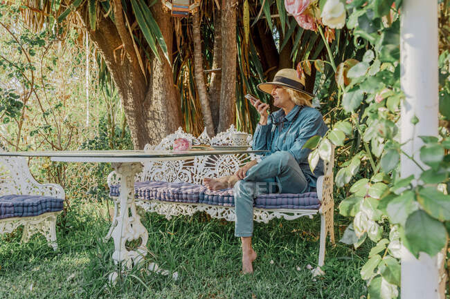 Seniorin sitzt auf Gartenbank und telefoniert — Stockfoto
