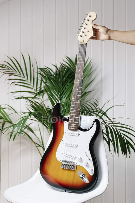 Image recadrée de la main de la femme tenant la guitare électrique sur la chaise à la maison — Photo de stock