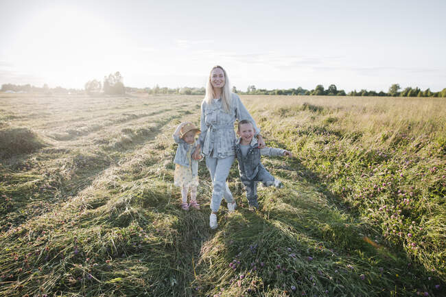 Sorridente madre con due bambini che camminano sul campo — Foto stock