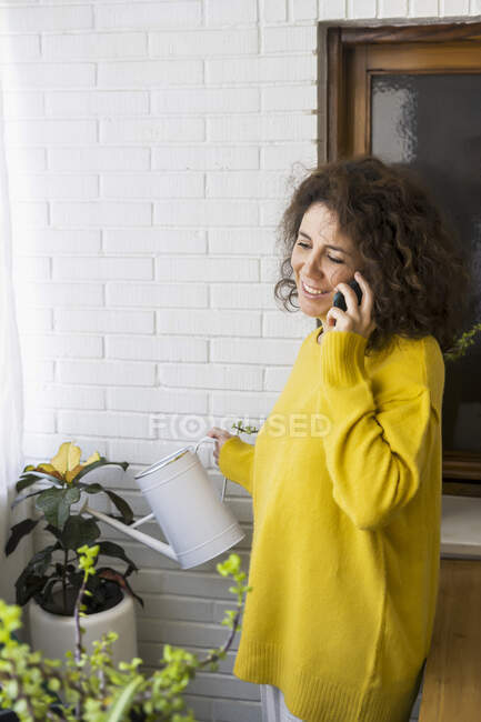 Frau telefoniert zu Hause und gießt Pflanzen — Stockfoto