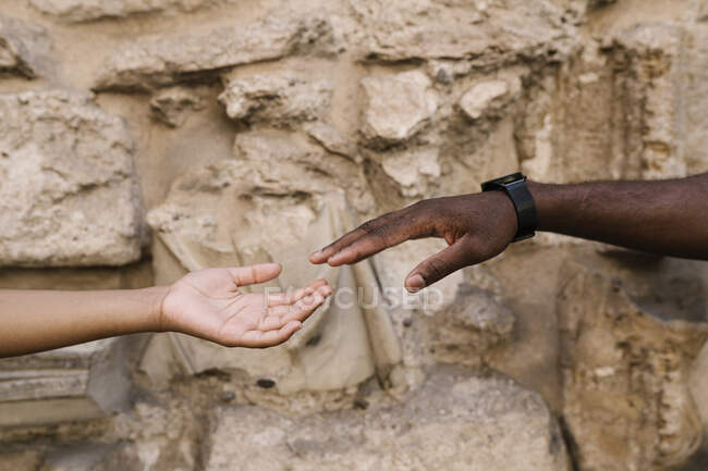 Cropped hands of couple reaching each other against stone wall — Stock Photo