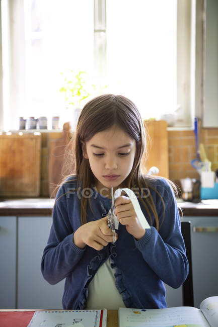 Девушка режет полоску бумаги во время домашнего задания — стоковое фото