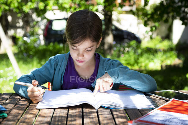 Mädchen sitzt am Gartentisch und macht Hausaufgaben — Stockfoto
