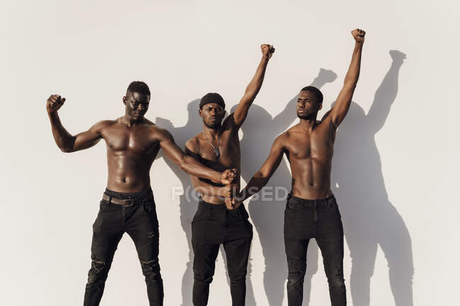 Trois hommes levant les poings pour protester, debout contre un mur blanc — Photo de stock