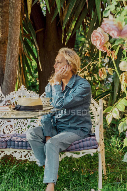 Porträt einer Seniorin, die auf einer Gartenbank sitzt und in die Ferne blickt — Stockfoto
