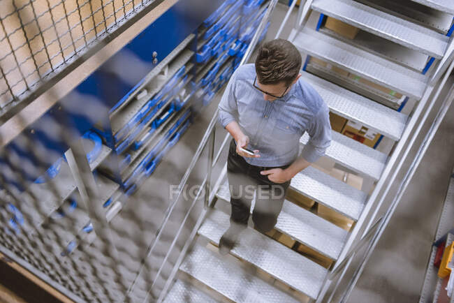 Бізнесмен за допомогою смартфона спускається по сходах на фабриці. — стокове фото