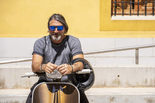 Mature man wearing sunglasses while sitting on motor scooter during sunny  day — lifestyle, sunlight - Stock Photo | #475186286