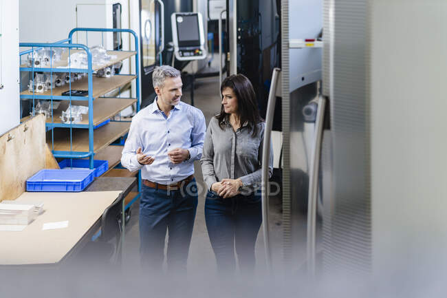 Empresario y empresaria caminando y hablando en una fábrica - foto de stock