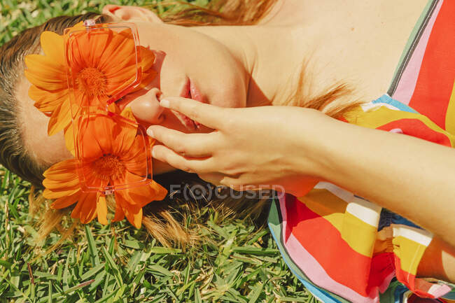 Portrait of woman lying on a meadow wearing glasses with orange flowers covering her eyes — Stock Photo