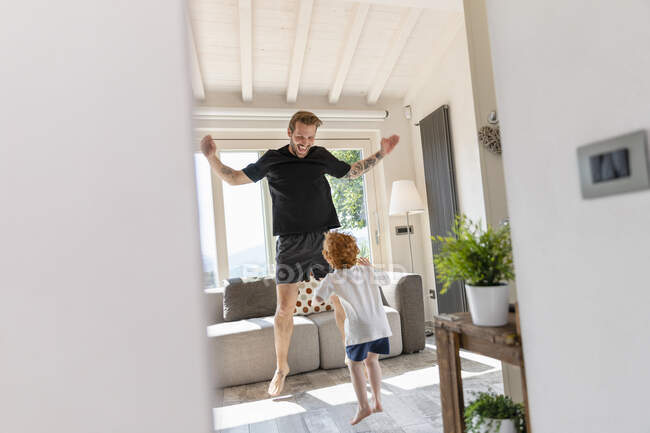 Alegre padre e hijo saltando mientras juega en la sala de estar en casa - foto de stock