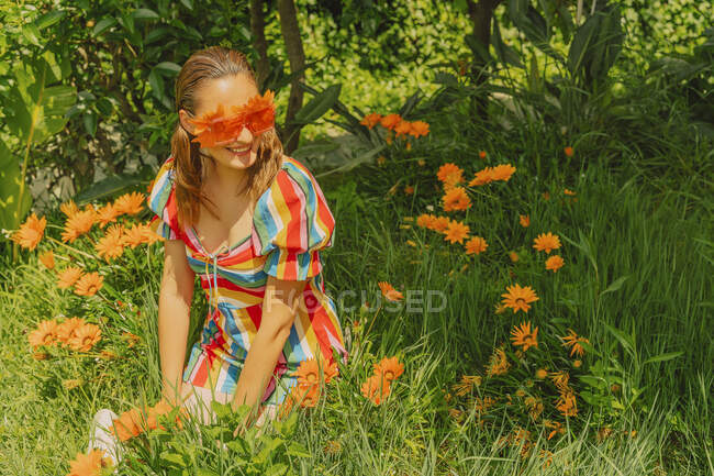 Portrait de femme heureuse dans la nature portant des lunettes avec des fleurs orange couvrant ses yeux — Photo de stock
