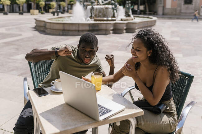 Happy couple gesturing during video call on laptop at sidewalk cafe — Stock Photo