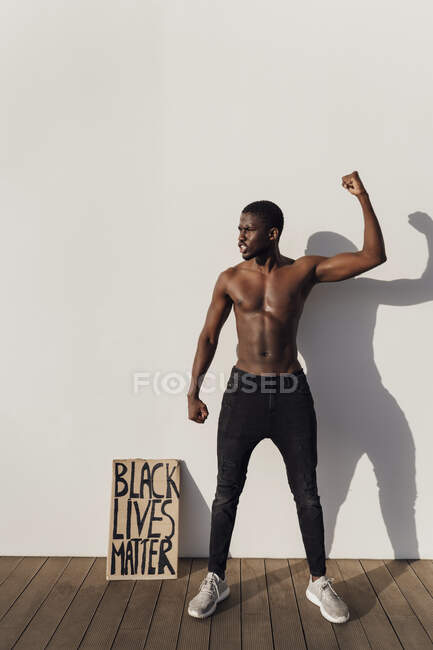 Чорний чоловік, що піднімає кулак з чорним кольором життя Знак матерії спирається на стіну — стокове фото
