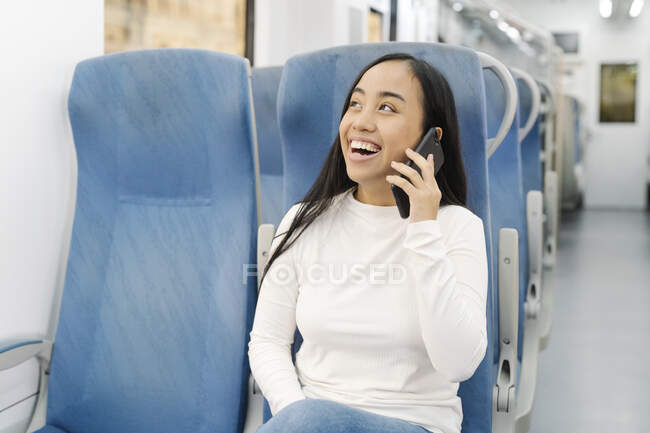 Cheerful young woman talking over smart phone while sitting on seat in train — Stock Photo