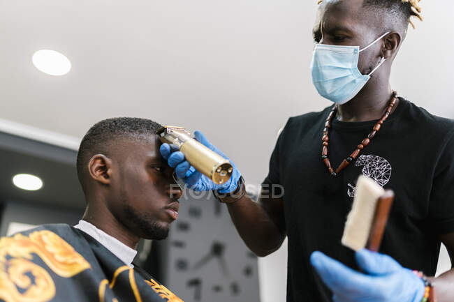Parrucchiere maschile con maschera taglio capelli cliente con rasoio in negozio di barbiere — Foto stock