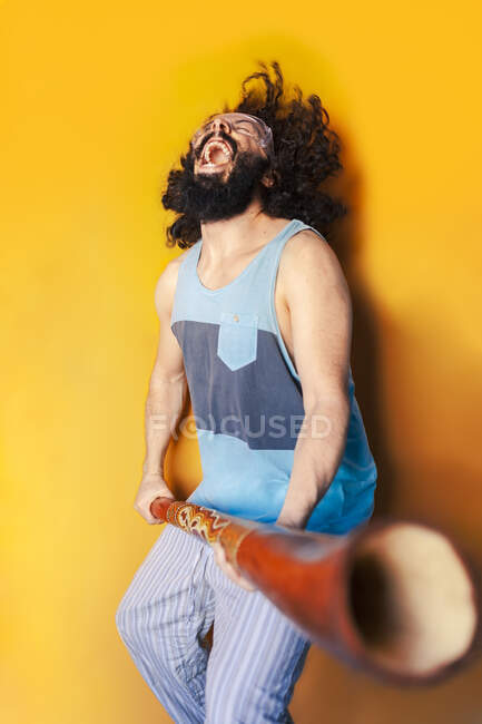 Crazy man holding didgeridoo laughing while standing against yellow  background — positive, music - Stock Photo | #475188312